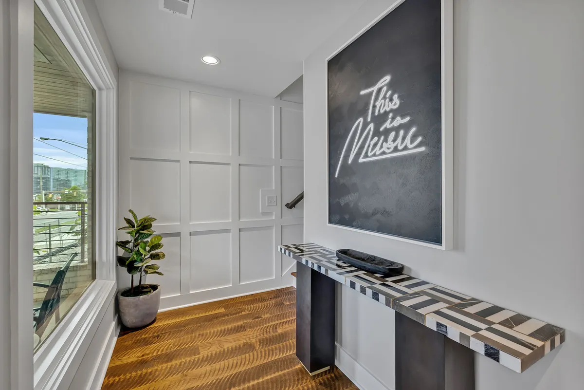 A modern and inviting entryway featuring a neon art piece, a stylish console table, and a large window, evoking a sense of welcome and creative detail upon entry.