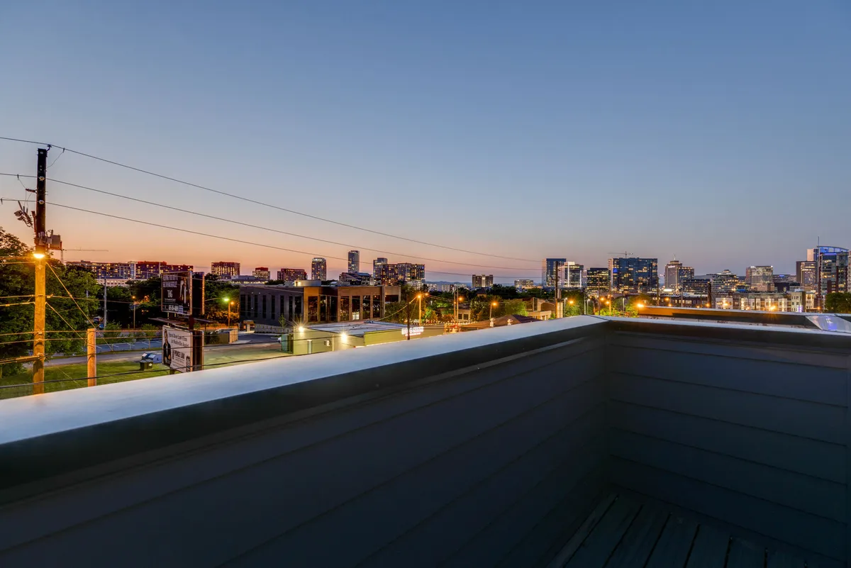 The image showcases a rooftop view with a city skyline at dusk, seen from behind a rooftop railing. The sky is tinted with sunset colors, and the atmosphere is serene yet inviting—perfect for gatherings or evening relaxation.