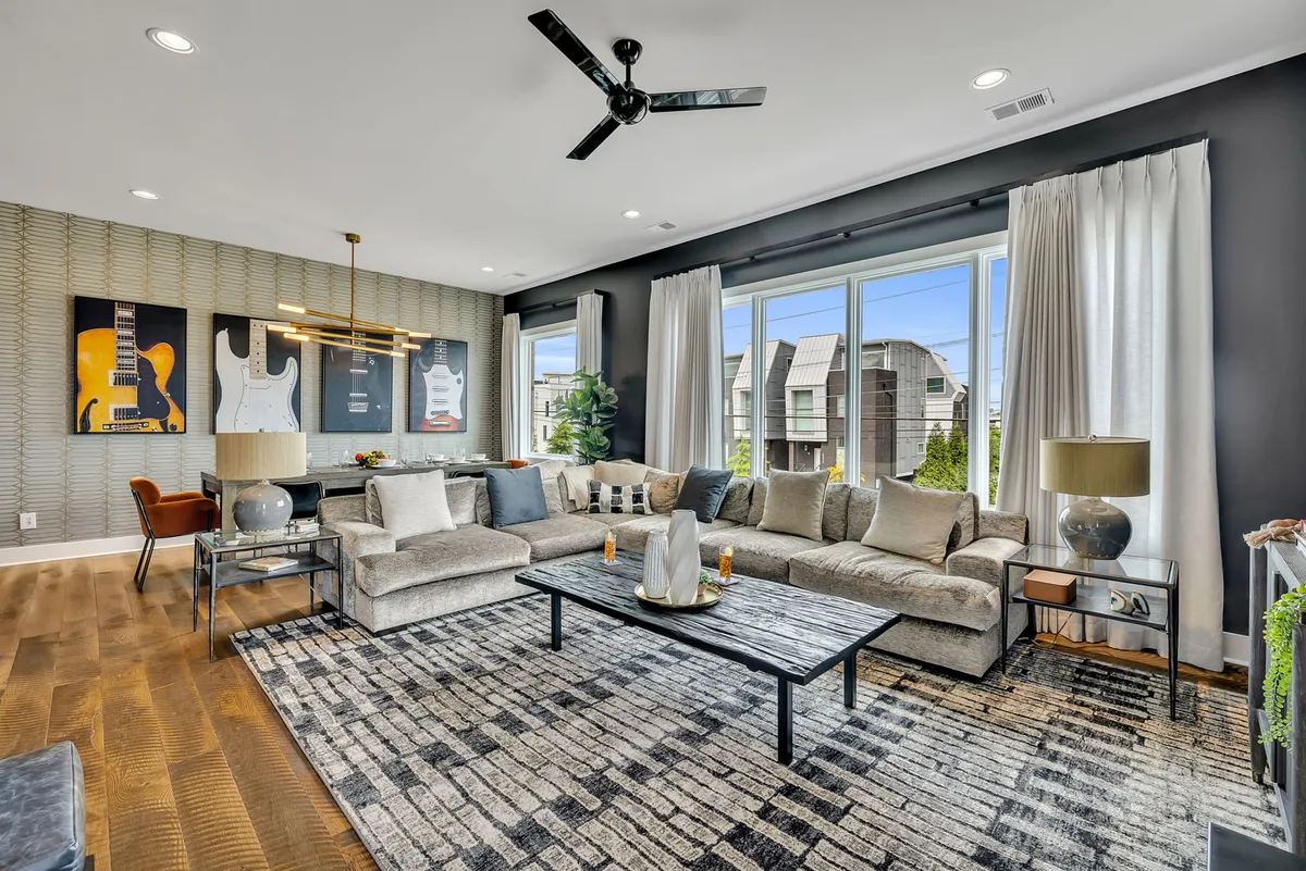 A contemporary living room featuring large sectional sofa, coffee table, and distinctive guitar art pieces on the wall. The space radiates a relaxed energy, perfect for socializing or unwinding, with ample room for gatherings around the modern décor.