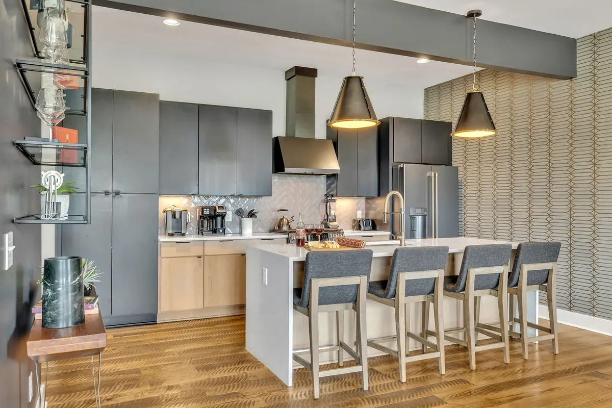 A modern kitchen with a spacious island, sleek bar stools, stylish cabinetry, and premium appliances. The area is brightly lit and designed for both cooking and entertaining, offering plenty of room for culinary creativity and casual gatherings.