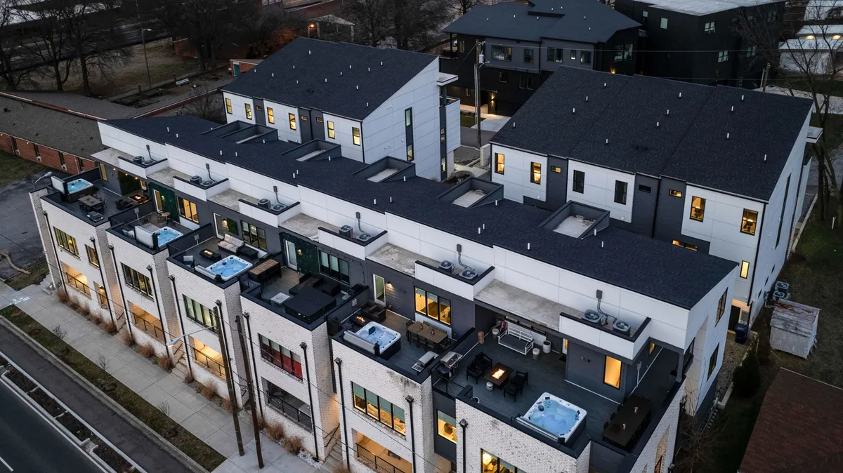 A contemporary rooftop setting showcases multiple hot tubs, sleek outdoor seating areas, and modern architectural details. The space is lively, designed for socializing and evening relaxation, with the city skyline visible beyond the deck. The inviting ambiance makes it ideal for gatherings and memory-making.
