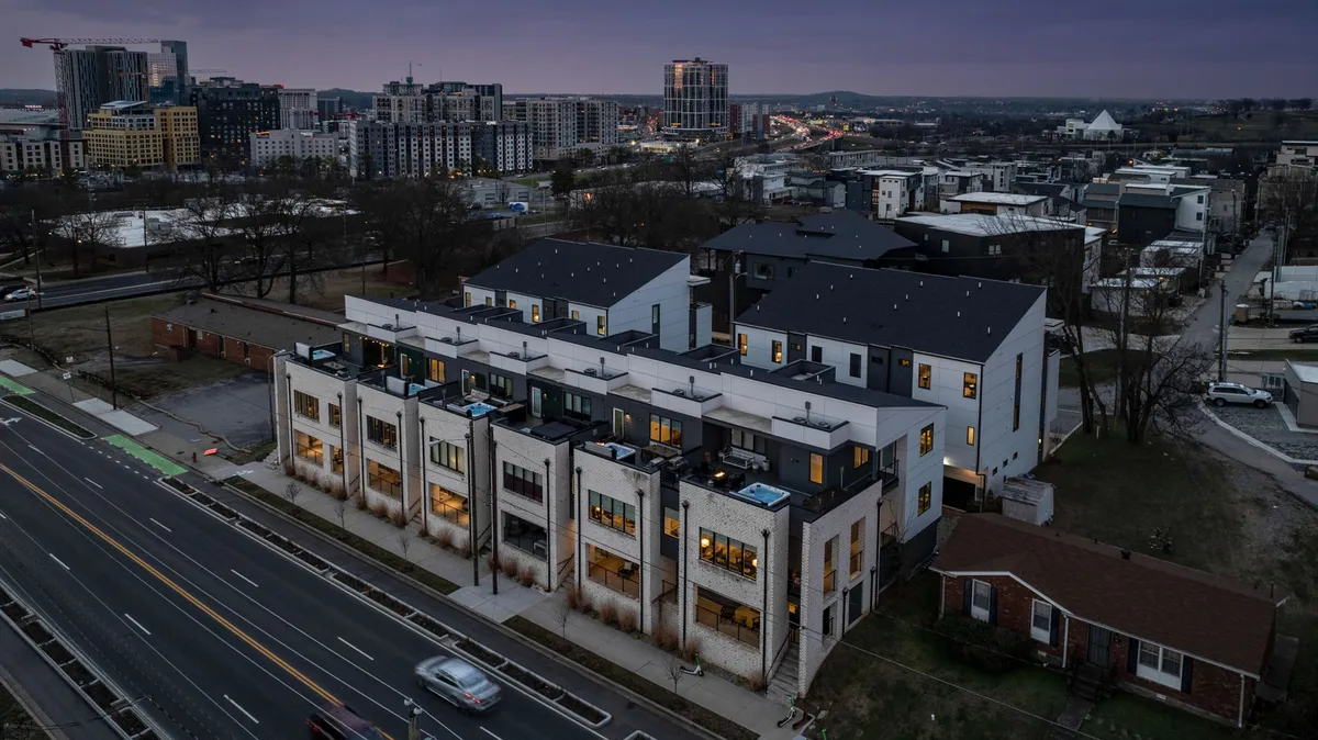 Contemporary townhomes line a lively city street with cars and the Nashville skyline in the background, highlighting the property’s prime urban location and proximity to downtown amenities.