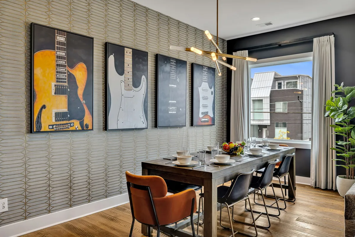 A dining area anchored by a stylish wooden table, surrounded by modern chairs, and illuminated by an eye-catching lighting fixture. Guitar-themed artwork adorns the wall, blending Nashville’s creative spirit with a welcoming setting for shared meals and celebrations.